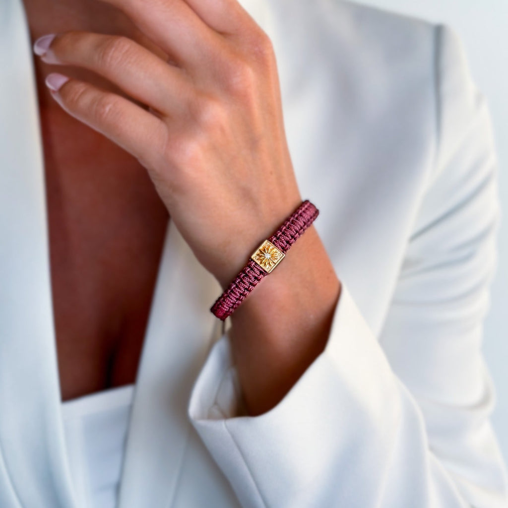 woman with white suit wearing burgundy braided  bracelet in gold 