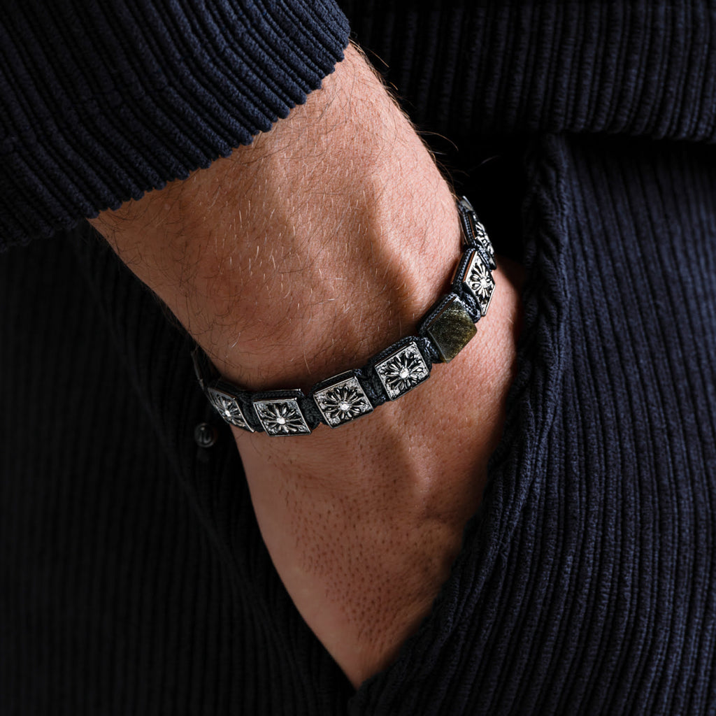 Close-up of a person wearing a black macrame bracelet with silver square designs.