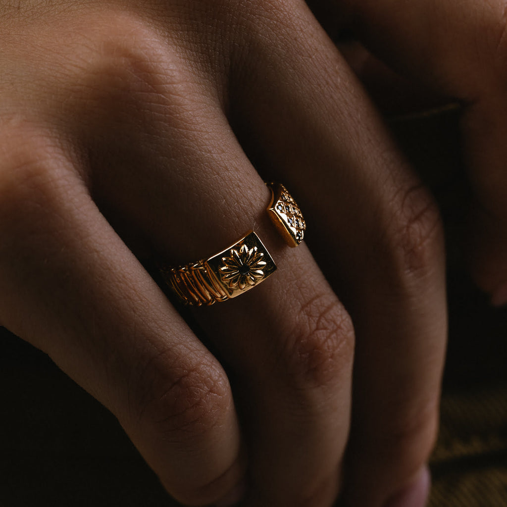 Close-up of a hand wearing a gold ring with black gemstones.