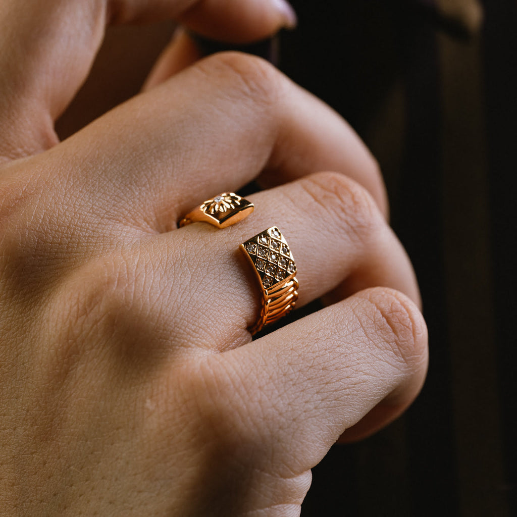 Close-up of a hand wearing gold ring with white gemstones on a dark background
