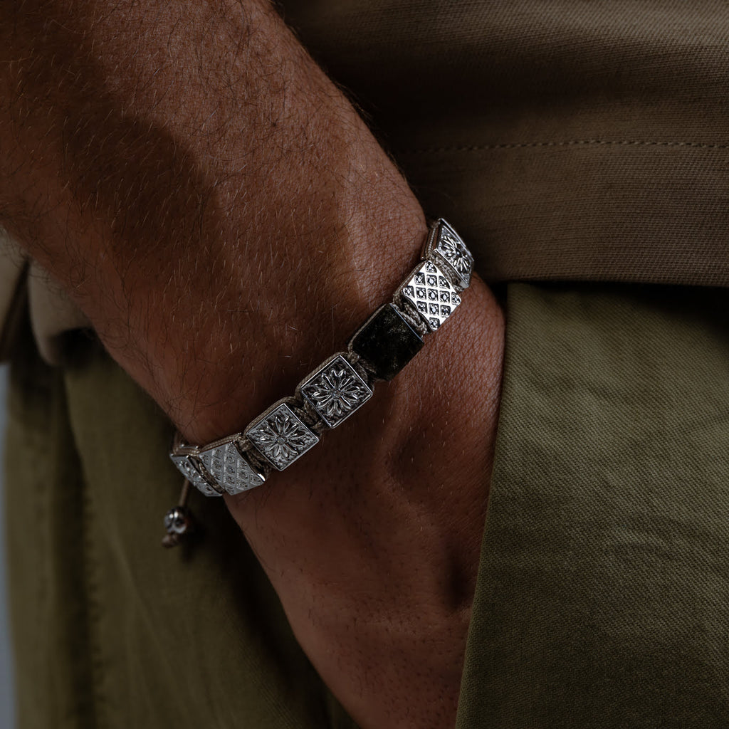Close-up of a person wearing a silver bracelet with geometric designs on a brown background