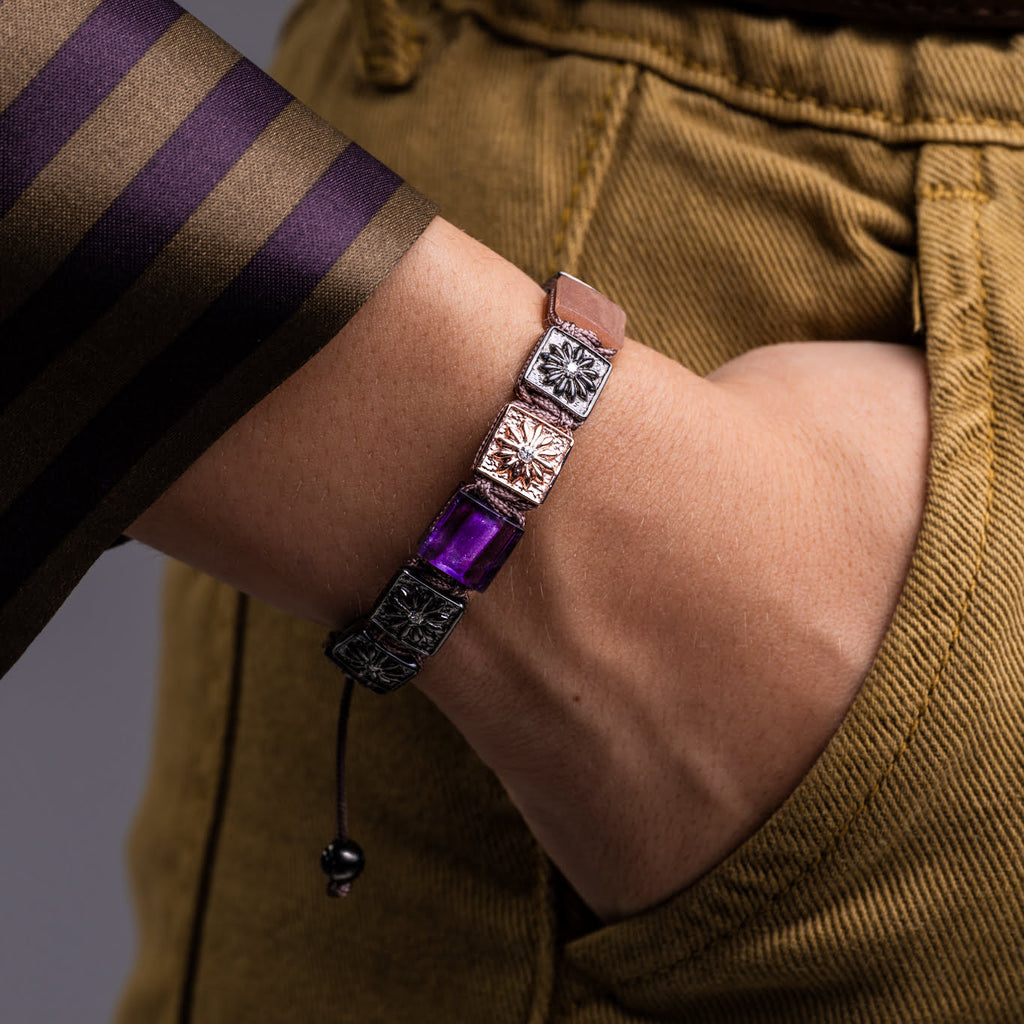 A bracelet with a purple gemstone on a wrist, worn by a person in a brown shirt.