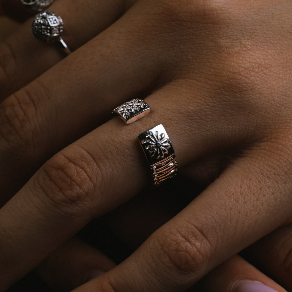Close-up of a hand wearing two silver rings with intricate designs.