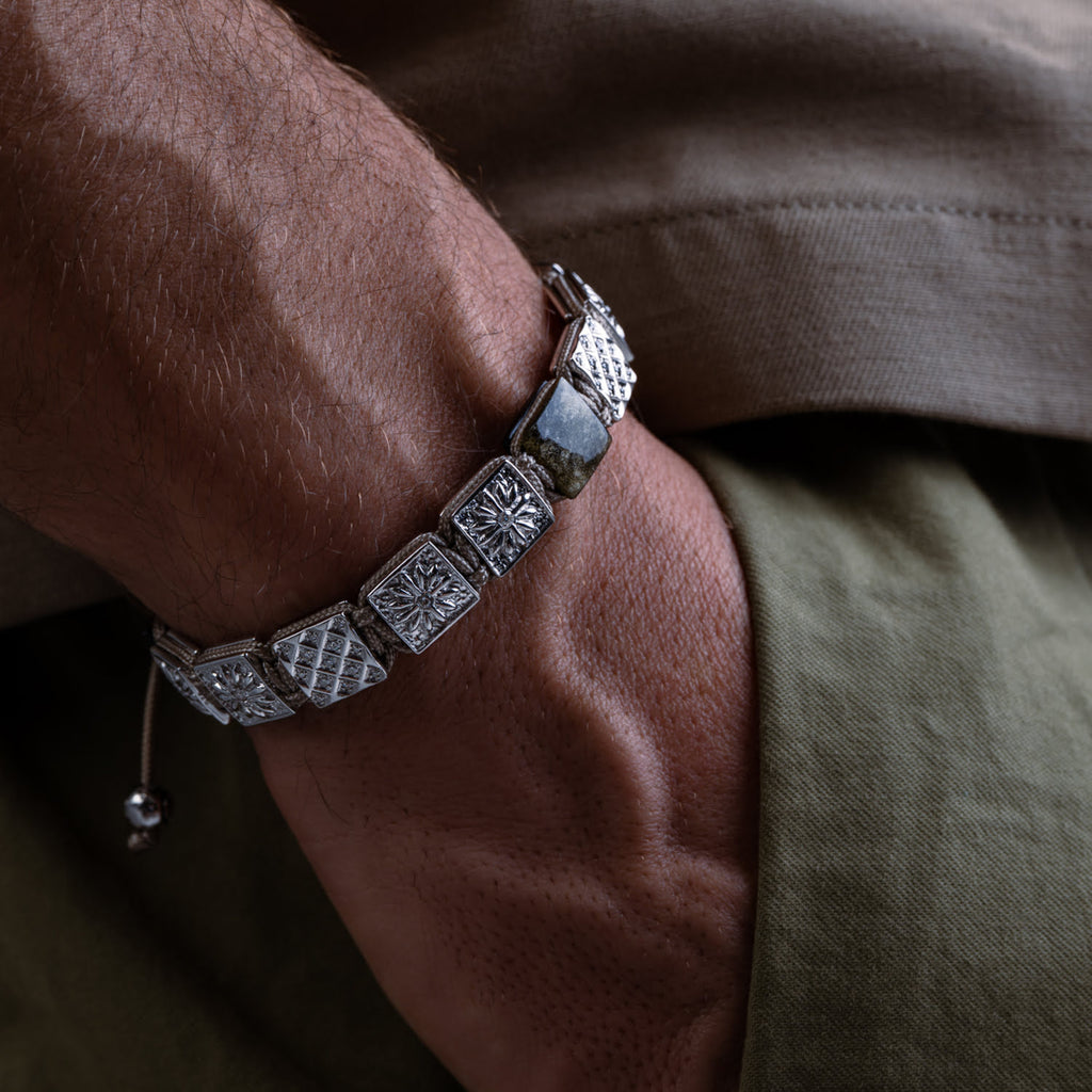 Silver bracelet with diamond-like patterns on a wrist against a neutral background