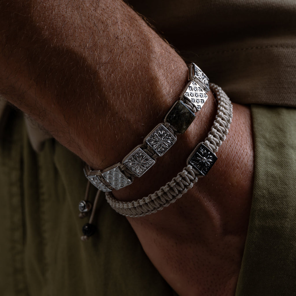 Close-up of a wrist wearing a bracelet with silver square beads on a brown background
